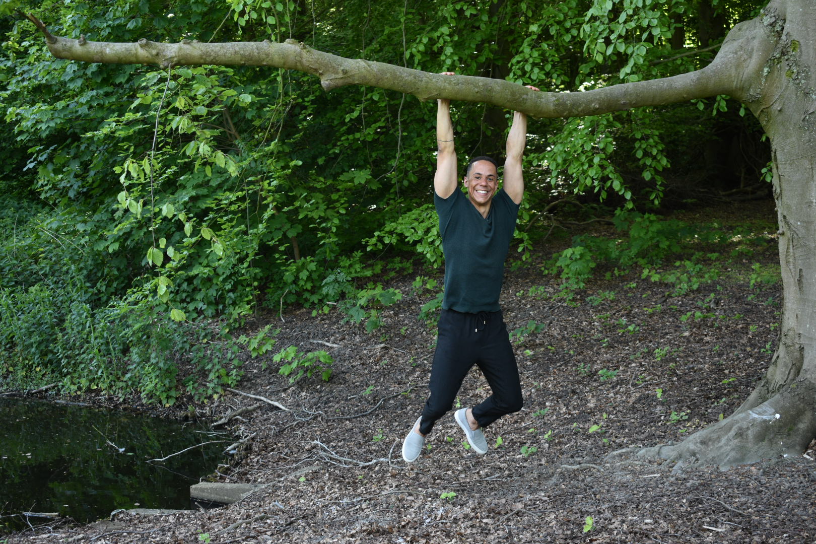 Yannick hangt lachend aan een boomtak in een groen boslandschap.