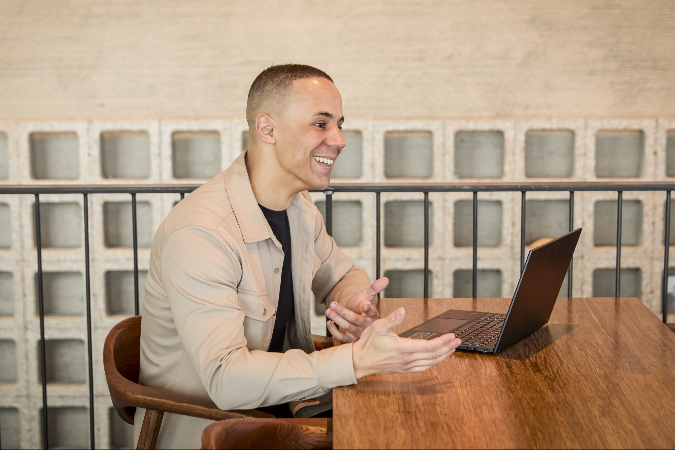 Yannick, zittend aan een houten tafel, lacht tijdens een videosessie achter zijn laptop in de moderne ruimte van Trainergy.