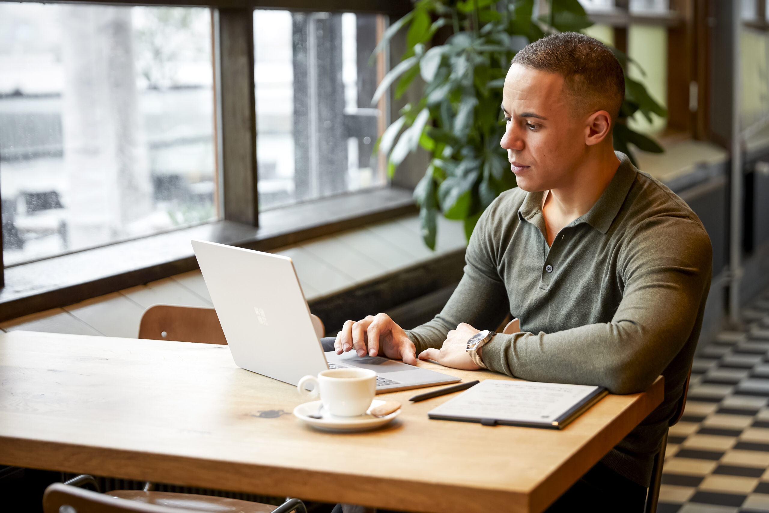 Yannick zit geconcentreerd te werken op een laptop aan een tafel in een gezellige caféomgeving.