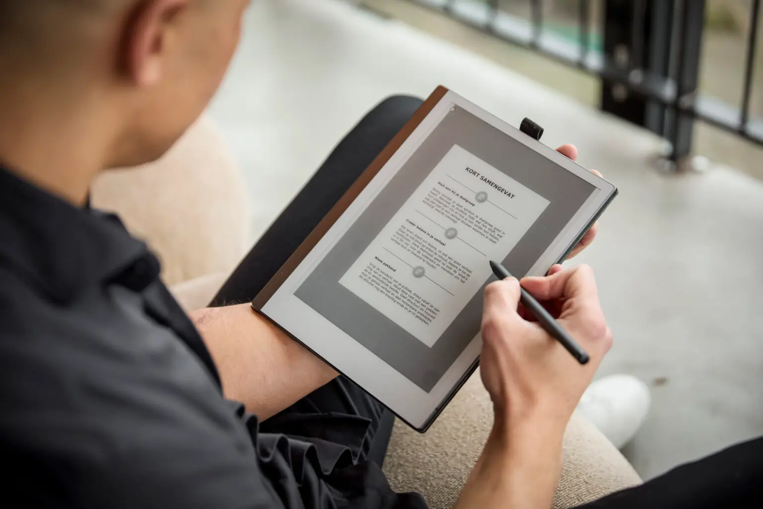 Yannick schrijft met een stylus op een digitaal notitieblok terwijl hij comfortabel zit.
