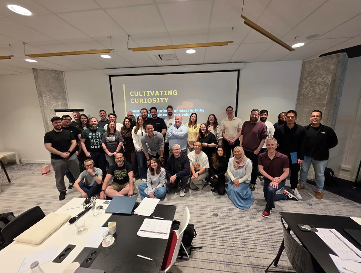 Groep professionals poseert samen voor een presentatie met de titel "Cultivating Curiosity" tijdens een bedrijfsworkshop.