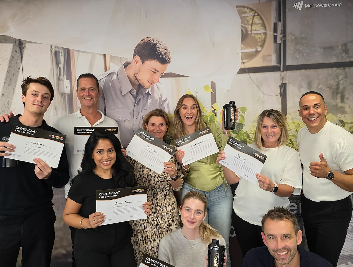 Een groep vrolijke mensen toont hun certificaten tijdens een evenement van Trainergy en ManpowerGroup.