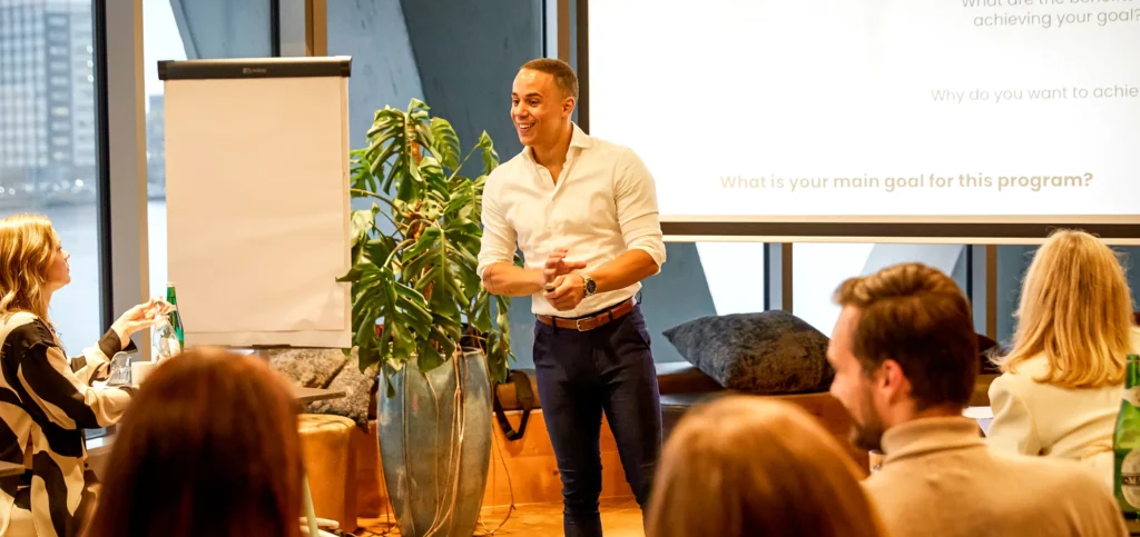 Een enthousiaste presentator, Yannick, leidt een sessie voor een groep mensen in een moderne vergaderruimte.