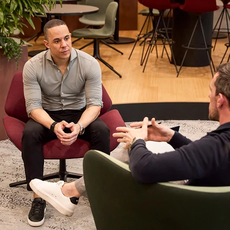 Twee mannen in moderne kantooromgeving voeren een gesprek in lounge stoelen.